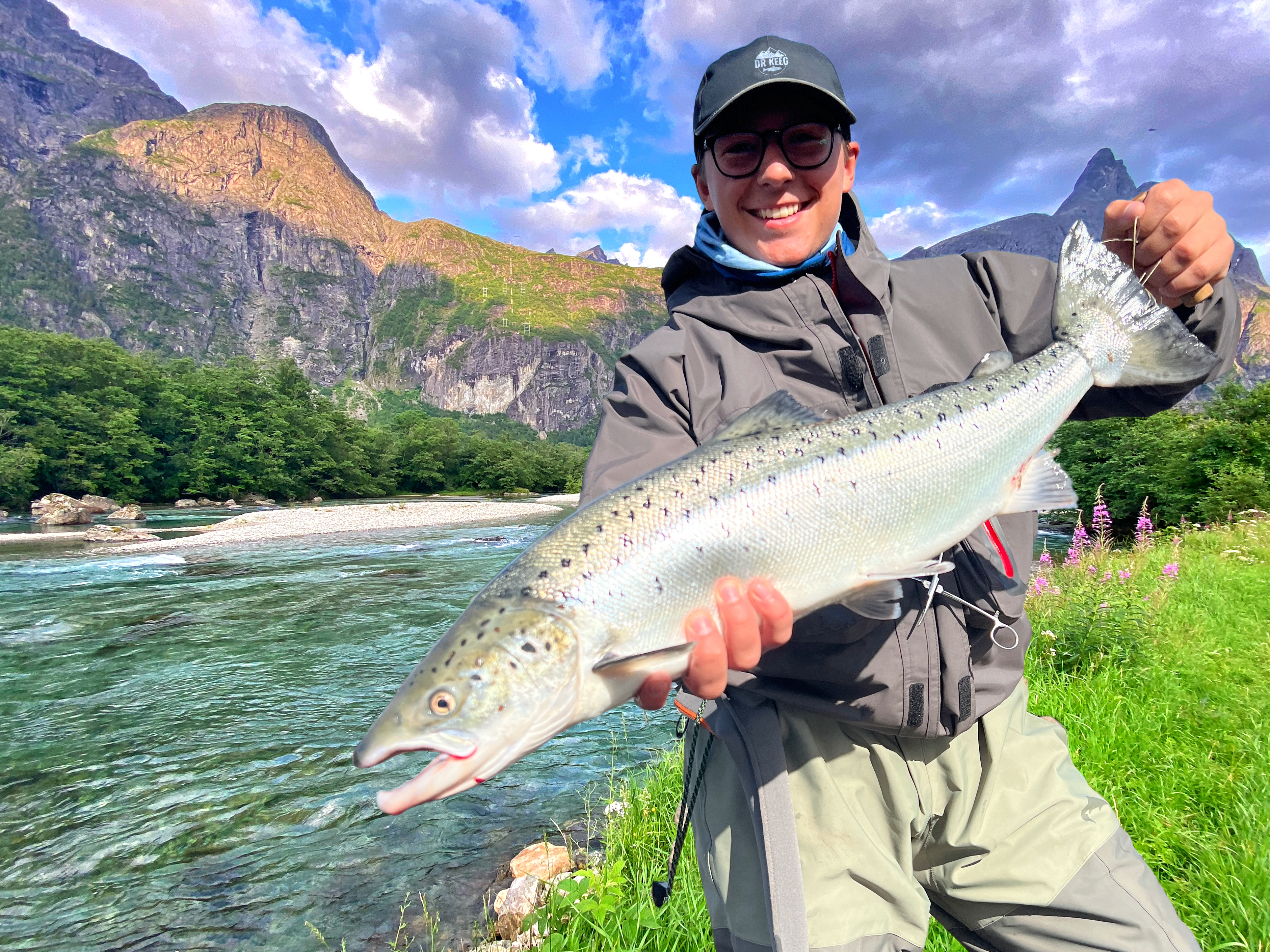 Man holding a bright salmon with dramatic scandinavian nature in the background
